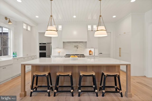 kitchen with decorative backsplash, custom range hood, double oven, white cabinetry, and a sink