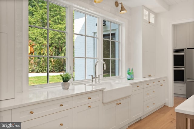 kitchen featuring light wood-style flooring, white cabinetry, light countertops, and a sink