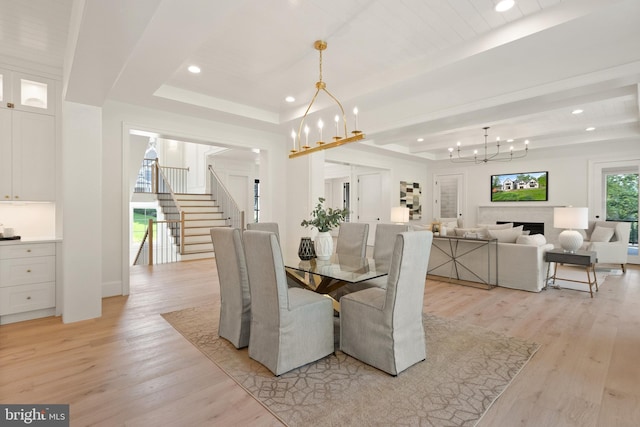 dining room with a tray ceiling, stairway, light wood-style floors, and a notable chandelier