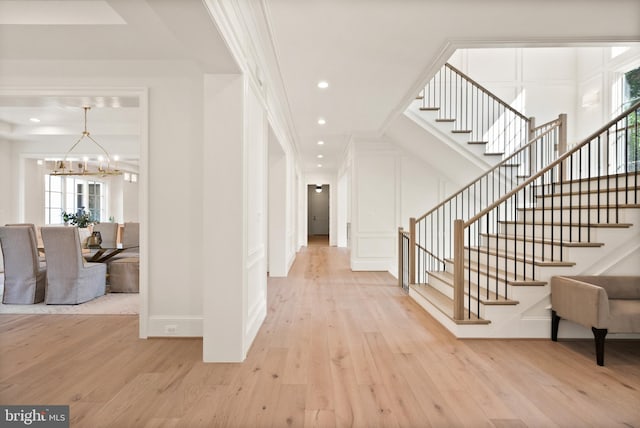 foyer featuring light wood-style floors, stairs, a decorative wall, and crown molding