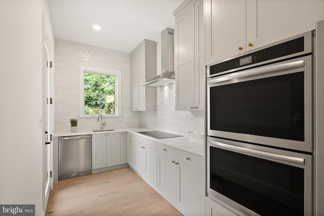 kitchen featuring backsplash, light wood-style flooring, appliances with stainless steel finishes, a sink, and wall chimney exhaust hood