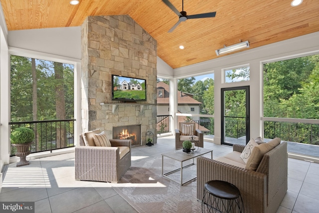 sunroom / solarium with wood ceiling, vaulted ceiling, a ceiling fan, and a stone fireplace