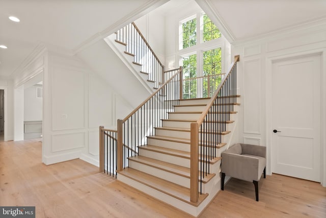 stairs with ornamental molding, wood finished floors, and a decorative wall