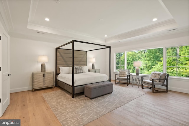 bedroom with ornamental molding, a tray ceiling, multiple windows, and light wood-style flooring