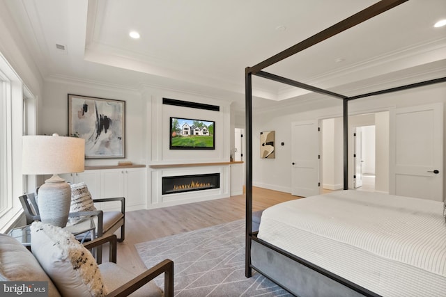 bedroom featuring light wood finished floors, a tray ceiling, ornamental molding, and a warm lit fireplace