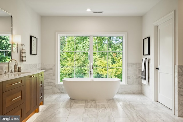 bathroom with tile walls, a soaking tub, visible vents, wainscoting, and vanity