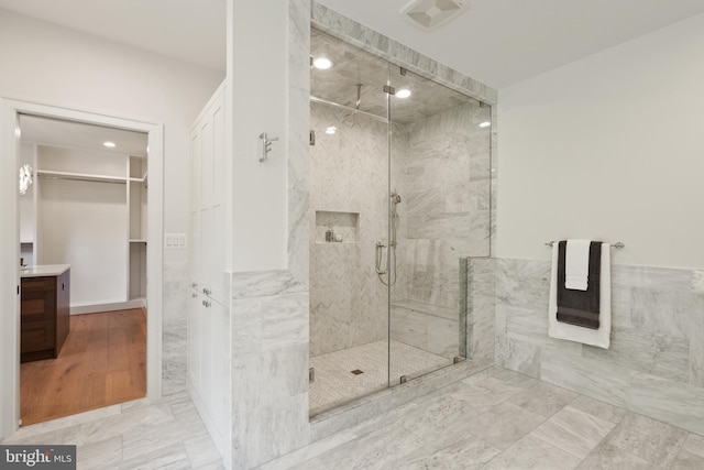 full bath featuring vanity, visible vents, tile walls, a spacious closet, and a marble finish shower