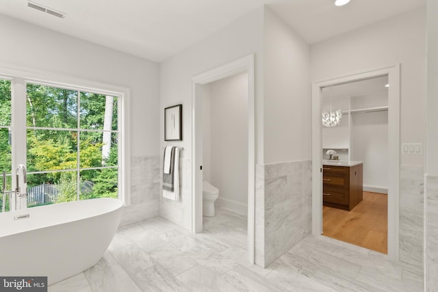 full bath with a freestanding tub, toilet, a wainscoted wall, visible vents, and tile walls