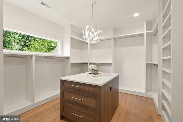 walk in closet with light wood finished floors, visible vents, and an inviting chandelier