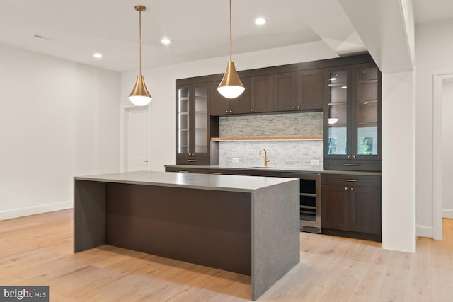 kitchen with light wood finished floors, backsplash, glass insert cabinets, a kitchen island, and dark brown cabinetry