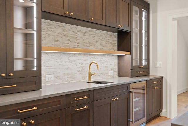 bar with wine cooler, light wood-style flooring, a sink, baseboards, and decorative backsplash