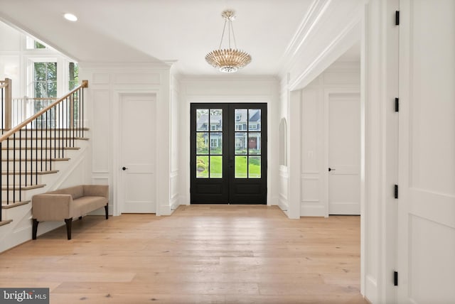 entrance foyer with ornamental molding, plenty of natural light, a decorative wall, and light wood finished floors