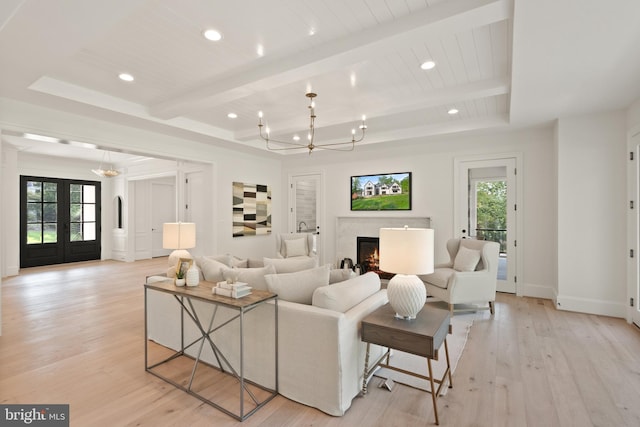 living room featuring a chandelier, light wood-type flooring, beamed ceiling, and a premium fireplace