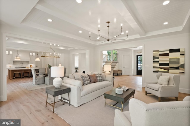 living room featuring stairs, a tray ceiling, light wood-type flooring, a chandelier, and beam ceiling