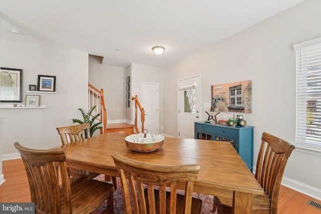 dining space featuring light wood-type flooring, visible vents, stairs, and baseboards