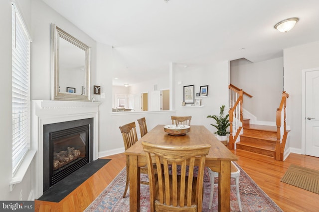 dining area with a fireplace with flush hearth, stairway, wood finished floors, and a healthy amount of sunlight