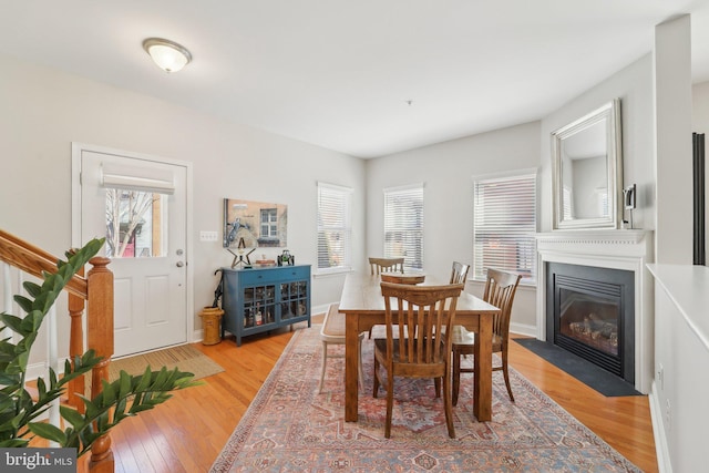 dining space with a fireplace with flush hearth, a healthy amount of sunlight, light wood-style flooring, and stairs