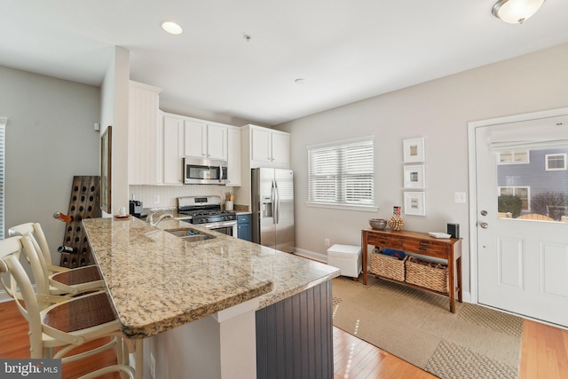 kitchen with appliances with stainless steel finishes, light stone counters, a peninsula, light wood-style floors, and a kitchen bar