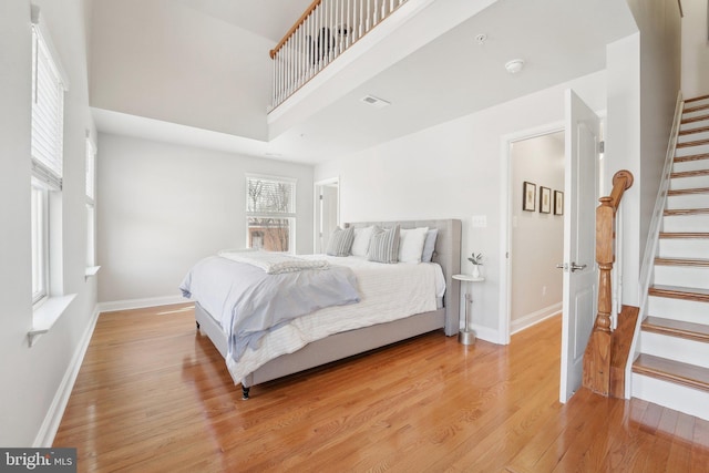 bedroom with light wood-type flooring, visible vents, a towering ceiling, and baseboards