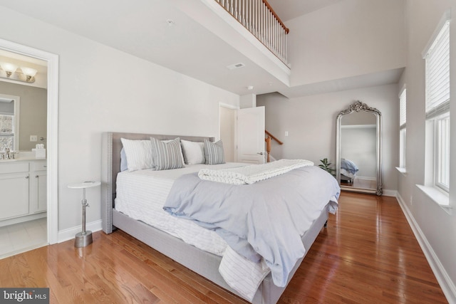 bedroom featuring visible vents, a towering ceiling, baseboards, and wood finished floors