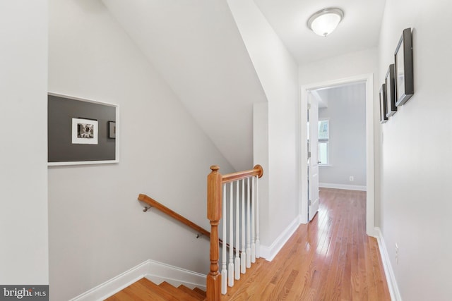 hallway featuring lofted ceiling, light wood-type flooring, an upstairs landing, and baseboards