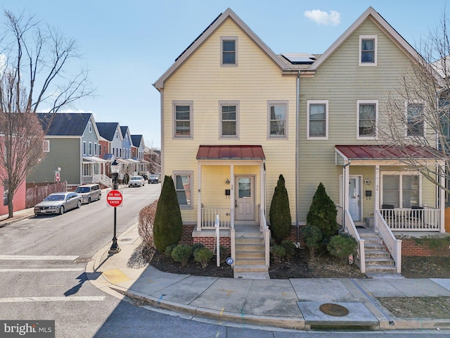 multi unit property with a residential view, metal roof, a standing seam roof, roof mounted solar panels, and a porch