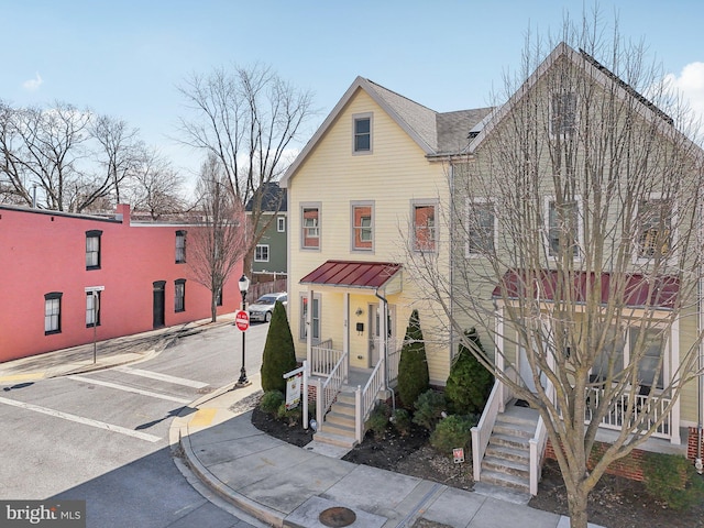 view of front of property with metal roof, a porch, a shingled roof, uncovered parking, and a standing seam roof