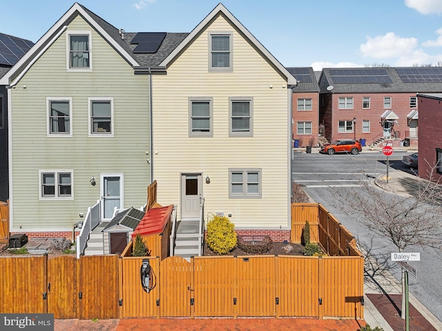 rear view of house with solar panels, central AC unit, a fenced front yard, and a gate