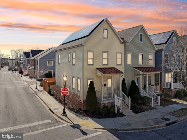 view of property featuring a residential view, metal roof, covered porch, a standing seam roof, and roof mounted solar panels