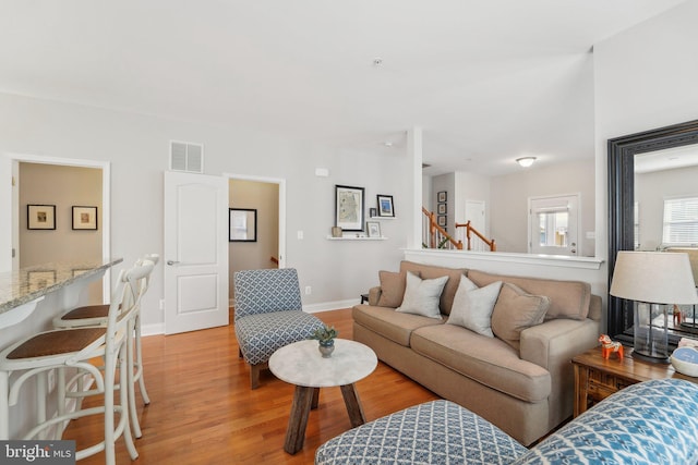 living area with light wood-style floors, visible vents, baseboards, and stairs