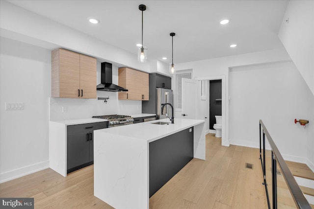 kitchen featuring stainless steel appliances, light countertops, a sink, modern cabinets, and wall chimney exhaust hood