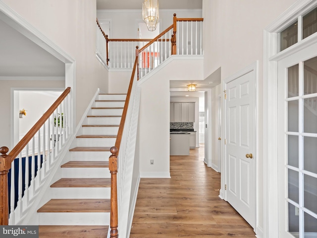 staircase with an inviting chandelier, wood finished floors, a towering ceiling, and crown molding