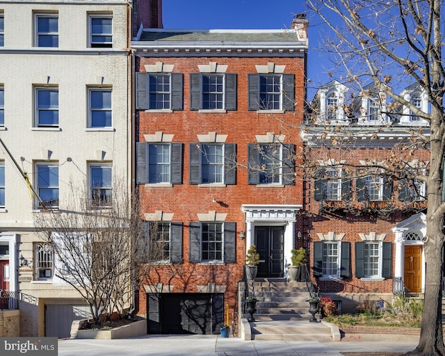 townhome / multi-family property featuring a garage, brick siding, driveway, and a chimney