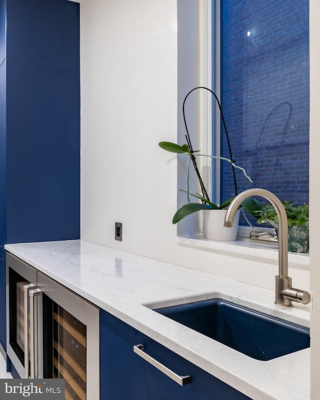 details featuring light stone counters, beverage cooler, a sink, bar, and blue cabinets