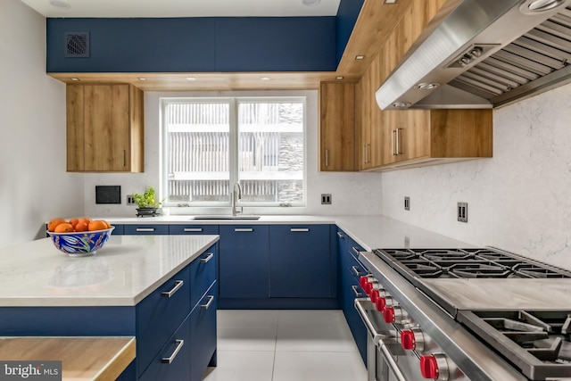 kitchen featuring visible vents, a sink, stainless steel stove, wall chimney range hood, and blue cabinets