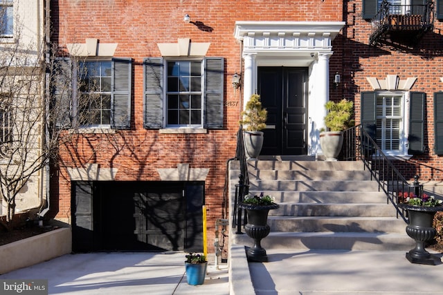 view of exterior entry with brick siding, concrete driveway, and a garage