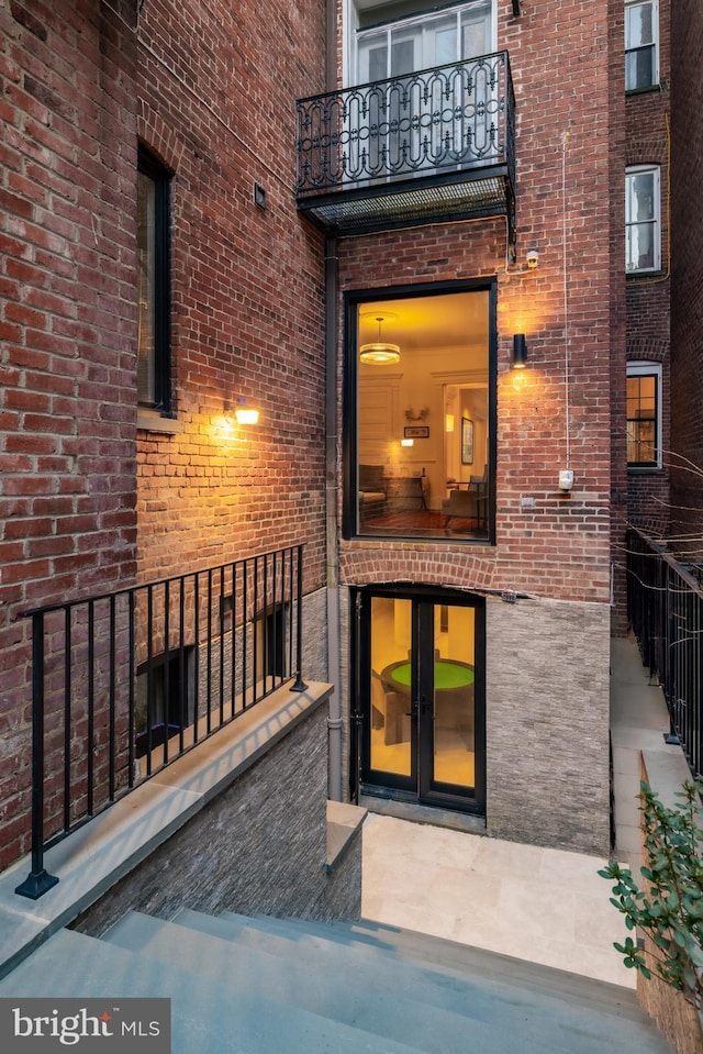 doorway to property with french doors, a balcony, and brick siding