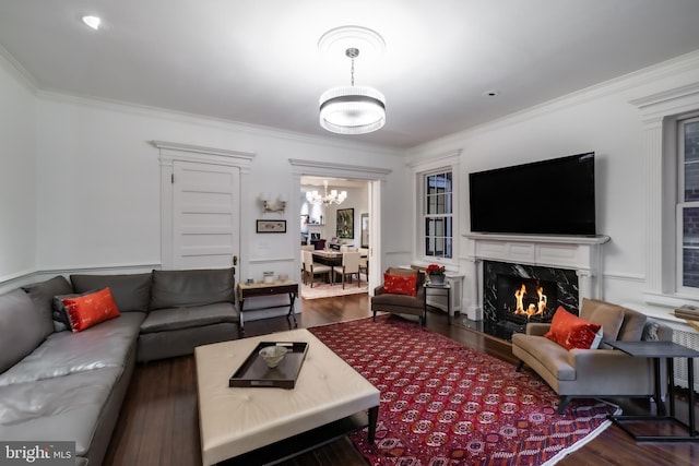 living room featuring wood finished floors, a notable chandelier, ornamental molding, and a high end fireplace