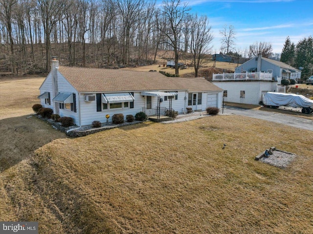 single story home featuring a garage, driveway, a chimney, a wall mounted air conditioner, and a front lawn