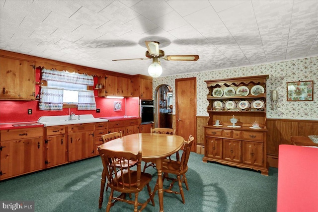 kitchen featuring oven, a wainscoted wall, light countertops, brown cabinets, and wallpapered walls