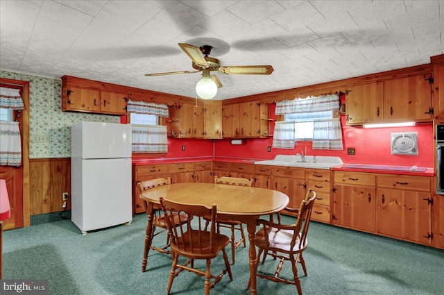 kitchen with wallpapered walls, brown cabinetry, a wainscoted wall, ceiling fan, and freestanding refrigerator