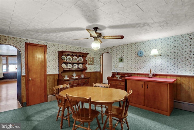 dining area with arched walkways, a baseboard heating unit, wainscoting, and wallpapered walls