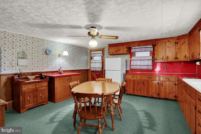 kitchen with brown cabinets, a wainscoted wall, freestanding refrigerator, carpet flooring, and wallpapered walls