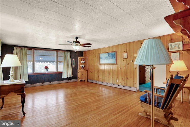 sitting room with ceiling fan, wood walls, baseboard heating, and wood finished floors