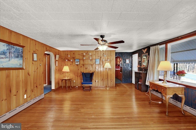 unfurnished room featuring a baseboard heating unit, arched walkways, a ceiling fan, and wood finished floors