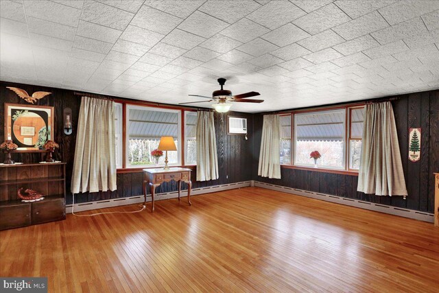 unfurnished living room with wood-type flooring, a wall unit AC, wood walls, and baseboard heating