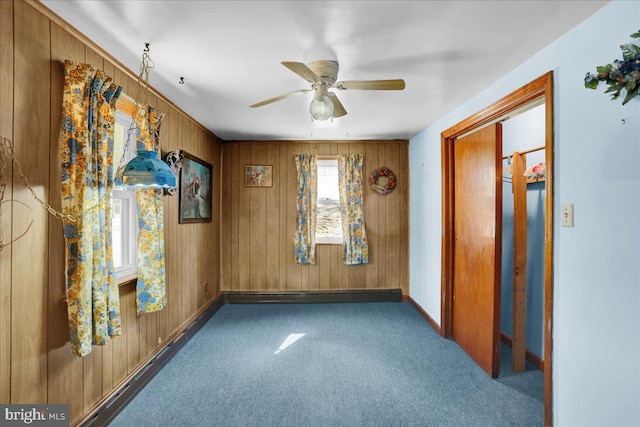 carpeted spare room featuring ceiling fan, wood walls, and baseboards