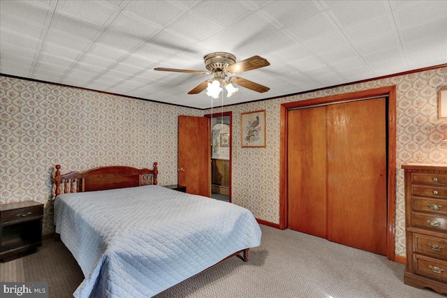 carpeted bedroom with ornamental molding, a closet, a ceiling fan, and wallpapered walls