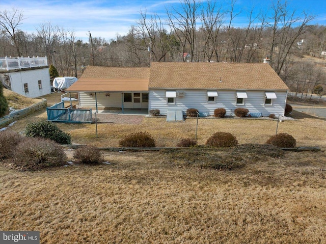 rear view of house with roof with shingles, a patio, and a chimney