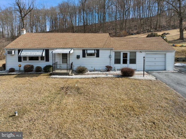 ranch-style house with driveway, a wall unit AC, a chimney, an attached garage, and a front lawn